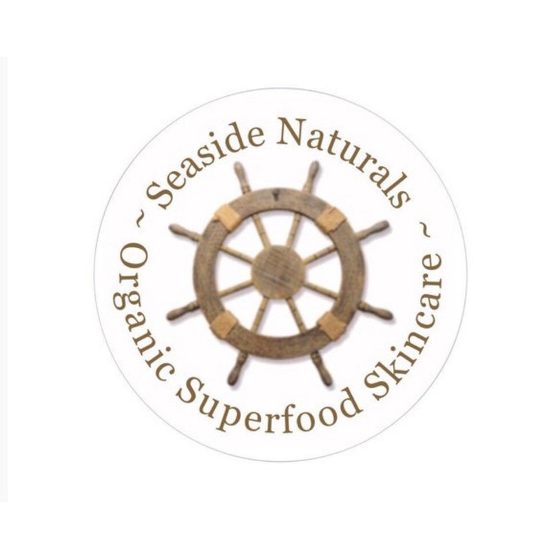 May include: A white circle with brown text that reads "~ Seaside Naturals ~ Organic Superfood Skincare". A wooden ship's wheel is in the center of the circle.