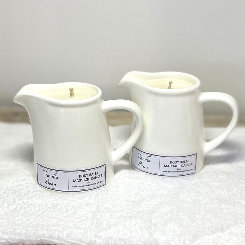 May include: Two white ceramic pitcher candles with a vanilla bean scent. The candles are labelled "Vanilla Bean" and "Body Balm Massage Candle".