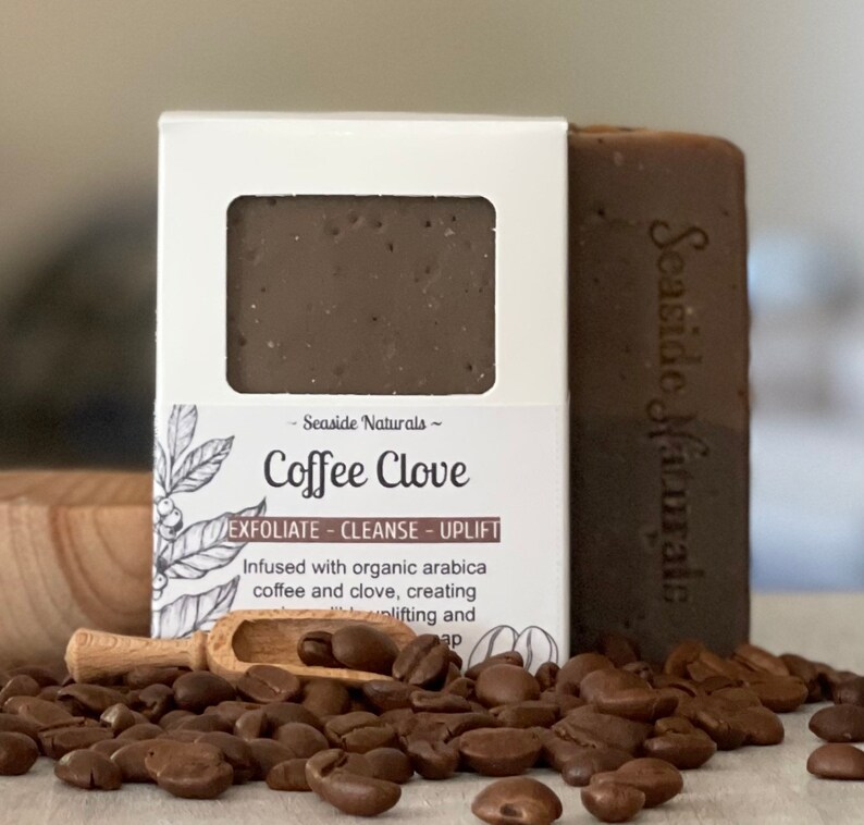 May include: A brown bar of soap with the text "Seaside Naturals - Coffee Clove" on the label. The soap is surrounded by coffee beans and a wooden scoop.
