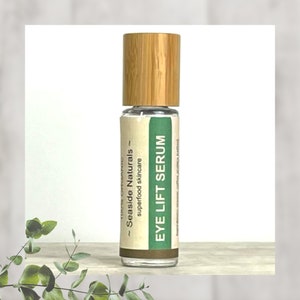 Puede incluir: Una botella de vidrio transparente con una tapa de madera marr&oacute;n y una etiqueta blanca que dice "100% Org&aacute;nico - Seaside Naturals - Cuidado de la piel con superalimentos - Suero para levantar los ojos".