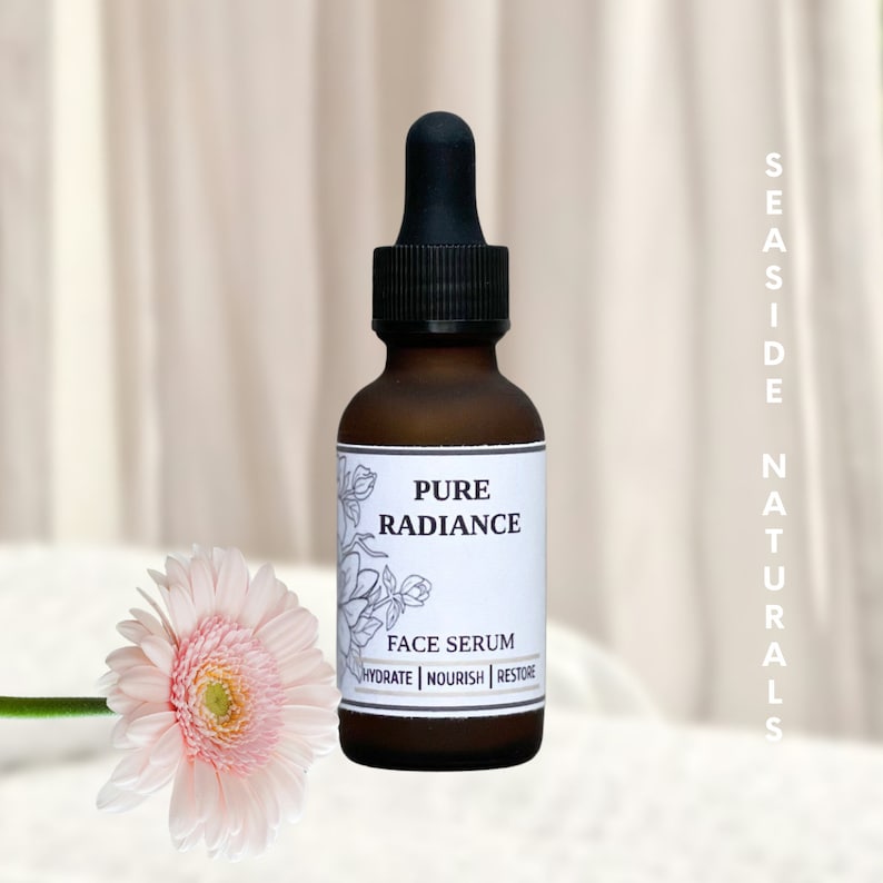 May include: A brown glass bottle with a black dropper top and a white label that reads "Pure Radiance Face Serum Hydrate | Nourish | Restore". The bottle is sitting on a white surface with a pink flower in the foreground.