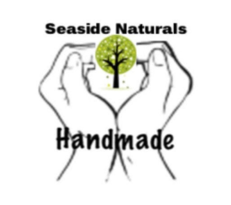 May include: A black and white logo with the words "Seaside Naturals" above the word "Handmade". The logo features a tree inside a green circle, held by two hands.