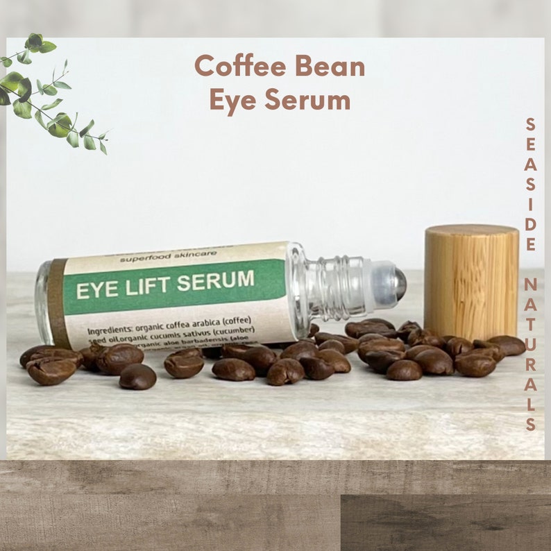Puede incluir: Un frasco de vidrio con rodillo con una etiqueta verde que dice "Eye Lift Serum" y una tapa de bamb&uacute;. El frasco est&aacute; rodeado de granos de caf&eacute; sobre una superficie de madera. La etiqueta tambi&eacute;n incluye el texto "superfood skincare" y enumera los ingredientes: coffea arabica org&aacute;nica (caf&eacute;), aceite de semilla de cucumis sativus org&aacute;nico (pepino), aloe barbadensis org&aacute;nico (aloe).