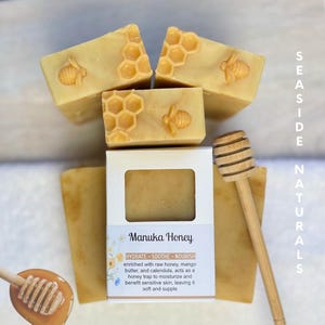 May include: Four bars of yellow soap with a honeycomb design and a bee image. The soap is in a white box with a label that reads "Manuka Honey" and describes the ingredients and benefits of the soap. A wooden honey dipper is also in the image.