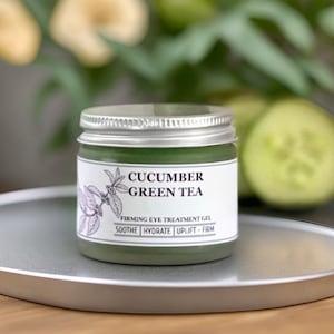May include: A small, round jar of green cucumber and green tea eye treatment gel. The jar has a silver lid and a white label that reads "Cucumber Green Tea Firming Eye Treatment Gel Soothe | Hydrate | Uplift - Firm"
