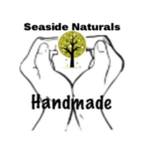 May include: Black and white illustration of two hands forming a heart shape around a stylized tree with yellow leaves. The text "SeaSide Naturals Handmade" is below the hands.