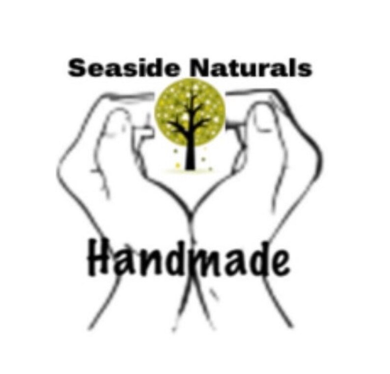 May include: Black and white illustration of two hands forming a heart shape around a stylized tree with yellow leaves. The text "SeaSide Naturals Handmade" is below the hands.