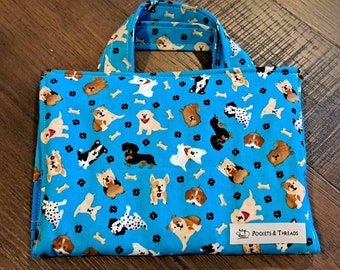 Puede incluir: Una bolsa de tela azul con un patrón de perros de dibujos animados y huesos. La bolsa tiene un asa y una etiqueta que dice "Pockets & Threads".