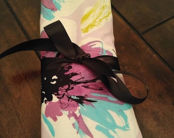 Puede incluir: Una bolsa de tela blanca con estampado floral en tonos rosa, azul y negro. La bolsa está atada con una cinta negra y tiene una etiqueta que dice "Pockets & Threads".