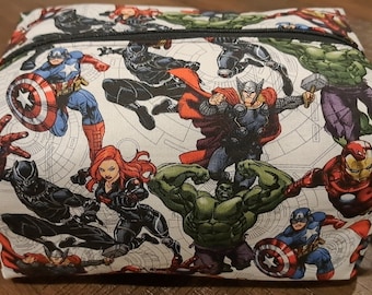 Puede incluir: Una bolsa de cosméticos de tela blanca con cierre de cremallera. La bolsa está cubierta con un estampado de varios superhéroes de Marvel, incluyendo Iron Man, Capitán América, Thor, Hulk, Viuda Negra y Pantera Negra.