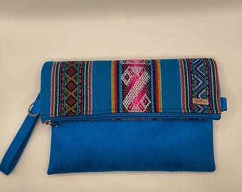 Puede incluir: Un bolso de mano turquesa con un colorido estampado tejido en la solapa. El bolso de mano tiene un cierre de cremallera y una correa de muñeca. El estampado tejido incluye diseños geométricos rosas, rojos, amarillos y azules. El bolso de mano está hecho de un material suave, similar al fieltro.