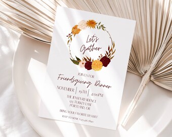 Puede incluir: Una tarjeta blanca con un diseño de corona de flores y el texto "Let's Gather" en una fuente marrón. La tarjeta es una invitación a una cena de Friendsgiving el 19 de noviembre a las 4:00 PM. La invitación incluye la dirección y pide a los invitados que traigan su postre favorito.
