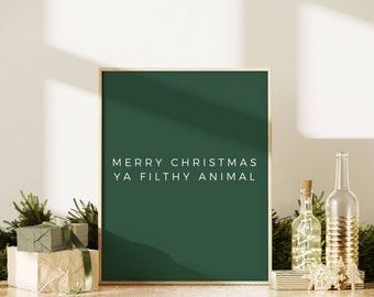 May include: A green framed print with the text "Merry Christmas Ya Filthy Animal" in white lettering. The print is sitting on a table with a few decorative items.