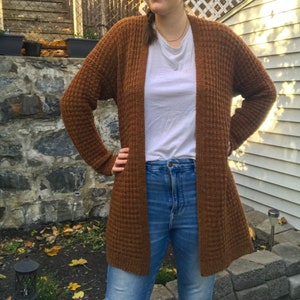 May include: A brown waffle knit cardigan with long sleeves and a relaxed fit. The cardigan is open in the front and has a slightly longer length.