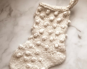 May include: A white knitted Christmas stocking with a textured bobble stitch pattern.