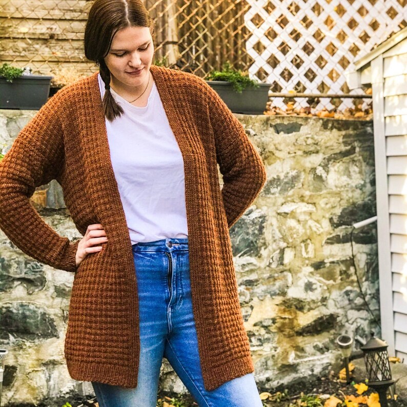 May include: A brown waffle knit cardigan with a long, open front. The cardigan is worn over a white t-shirt and blue jeans.