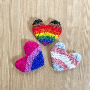 May include: Three knitted hearts in the shape of a rainbow, pink and blue stripes, and pink and white stripes.