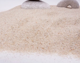 May include: A close-up of a pile of light brown sand with two smooth gray stones on top. The stones are round and have a natural, weathered look.