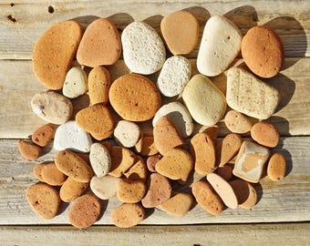 May include: A collection of smooth, naturally shaped stones in various sizes and shades of tan, brown, and white. The stones are arranged on a weathered wooden surface, creating a natural, earthy aesthetic.