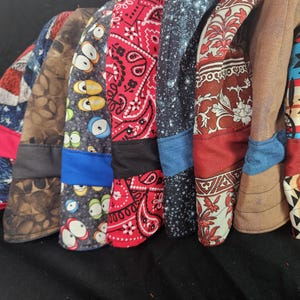 May include: A collection of eight fabric scrub caps arranged in a row, featuring diverse patterns including American flag stars and stripes, brown coffee beans, cartoon eyes, red paisley, starry night, floral motifs, solid tan, and geometric shapes.