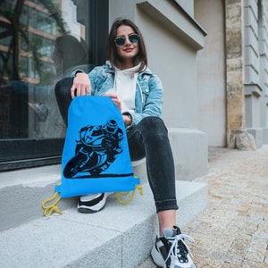 May include: A blue drawstring bag with a black silhouette of a person riding a motorcycle. The bag has yellow drawstrings.