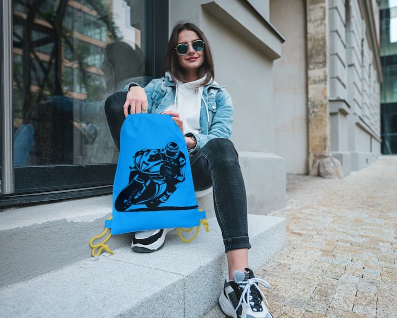 May include: A blue drawstring bag with a black silhouette of a person riding a motorcycle. The bag has yellow drawstrings.