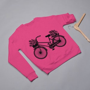 May include: A pink sweatshirt with a black silhouette of a bicycle with flowers in the basket.