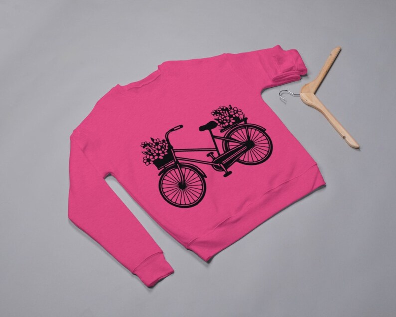May include: A pink sweatshirt with a black silhouette of a bicycle with flowers in the basket.