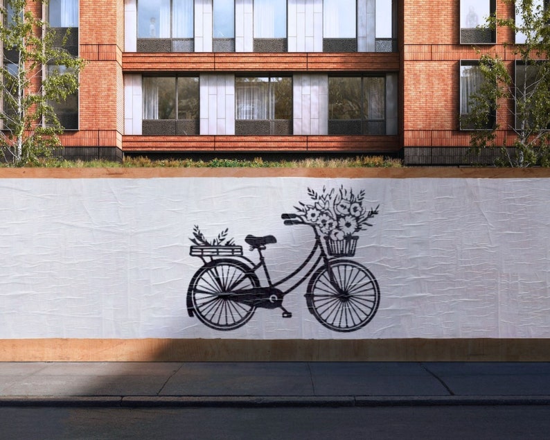 May include: A black bicycle with a basket of flowers on the handlebars. The bicycle is on a white background with a brick building in the background.