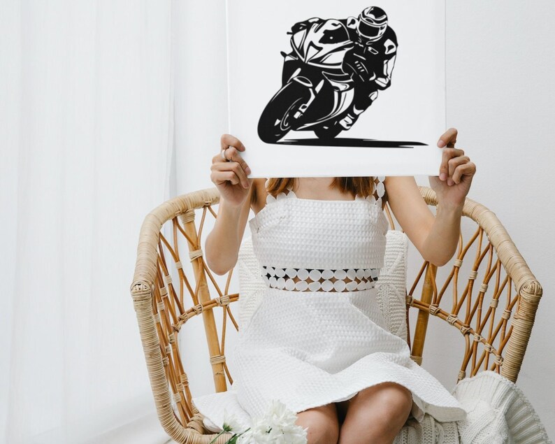 May include: A woman holds a white poster in front of her face. The poster features a black and white silhouette of a motorcycle racer riding a motorcycle.