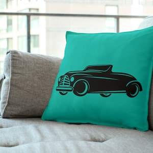 May include: A teal blue throw pillow with a black silhouette of a vintage car. The car has a convertible top and is facing to the right.