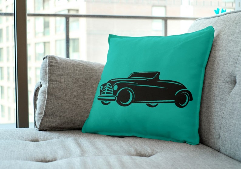 May include: A teal blue throw pillow with a black silhouette of a vintage car. The car has a convertible top and is facing to the right.