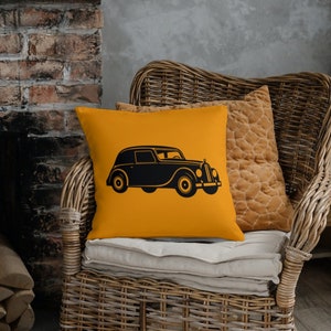 May include: A yellow throw pillow with a black silhouette of a vintage car. The pillow is sitting on a wicker chair.