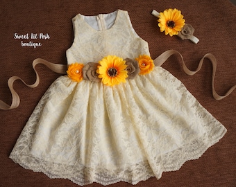 May include: A white lace dress with a sunflower and burlap flower belt and a matching sunflower headband. The dress has a scalloped hem and is perfect for a special occasion.