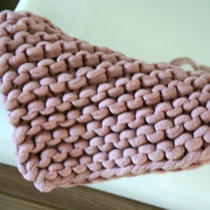 May include: A close-up of a pink knitted dishcloth. The dishcloth is made of thick yarn and has a textured surface.