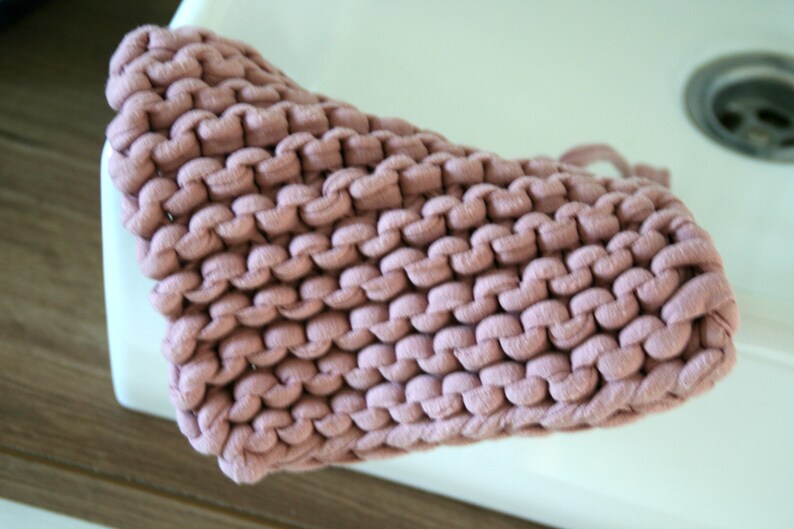 May include: A close-up of a pink knitted dishcloth. The dishcloth is made of thick yarn and has a textured surface.
