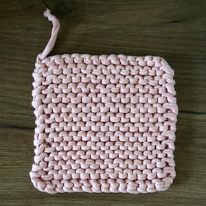 Op de afbeelding: Een roze gebreide pot onderzetter met een lus om op te hangen.