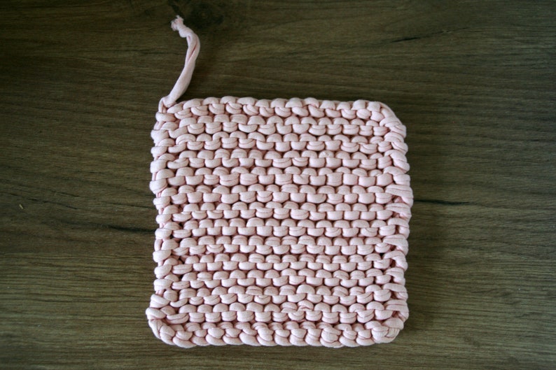 Op de afbeelding: Een roze gebreide pot onderzetter met een lus om op te hangen.