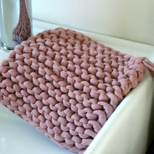May include: A soft, pink knitted washcloth with a knotted handle. The washcloth is sitting on a white porcelain sink.