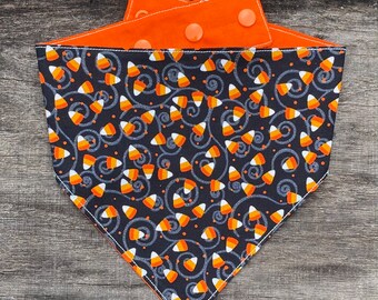 Puede incluir: Bandana reversible para mascotas con un diseño de caramelos de maíz sobre fondo negro. El reverso es naranja. Tiene cierres de botón a presión naranjas. Perfecto para Halloween.