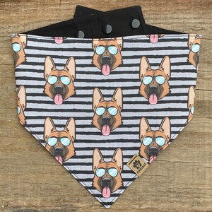 May include: A black and white striped dog bandana with a repeating pattern of German Shepherd dogs wearing sunglasses. The bandana has a black adjustable strap with two snap closures. The bandana has a brown leather tag with the text "FOUR PAWS" printed on it.