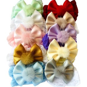 Puede incluir: Colección de diademas para bebés de colores. Cada diadema presenta un lazo de satén con un pompón esponjoso en el centro. Los colores incluyen rojo, dorado, azul, rosa y verde. Sobre un fondo blanco.