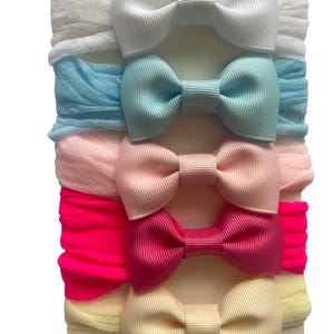 Puede incluir: Un conjunto de cinco diademas para bebés con lazos. Cada diadema presenta un lazo de diferente color: blanco, celeste, rosa, rosa fuerte y crema. Las diademas están hechas de tela suave y elástica.