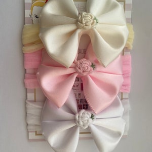 May include: Three satin headbands with bows and embroidered flowers. The headbands are in white, pink, and yellow.