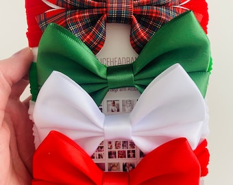 Puede incluir: Un conjunto de cuatro lazos para el cabello de colores. El lazo superior presenta un estampado de cuadros rojos y verdes. Debajo hay lazos en verde, blanco y rojo. Los lazos están sujetos a bandas elásticas. Sobre un fondo blanco.