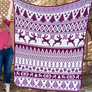 May include: A large, rectangular blanket with a white and claret geometric pattern. The design includes reindeer, trees, and diamond shapes. The blanket is held up against a wooden fence and a tree.