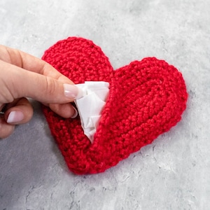 May include: A red crocheted heart-shaped pouch with a white tissue inside. The pouch is open and the tissue is partially visible.