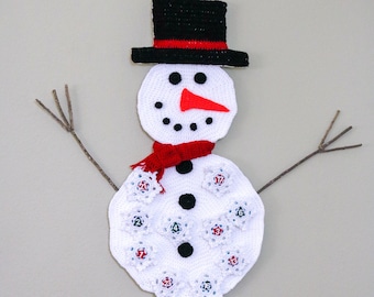 May include: White crocheted snowman advent calendar with 24 numbered circles. The snowman has a black top hat, red scarf, and black buttons. The snowman is hanging on a wall.
