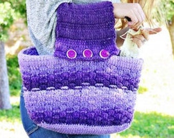May include: A purple and lavender crocheted tote bag with a purple crocheted strap and three purple buttons. The bag is being held by a person wearing a grey sweater.