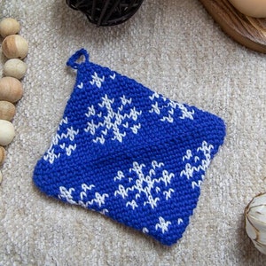 Puede incluir: Un agarrador de olla de punto azul con un patrón de copo de nieve blanco.